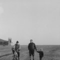 Spaziergänger (Eberhard Hanusch mit seinem Sohn) und Mopedfahrer (Herr Breunig) auf dem Grasberg, hinten links das erste Flugplatzgebäude des Vereins, laut Fotorückseite von 1963